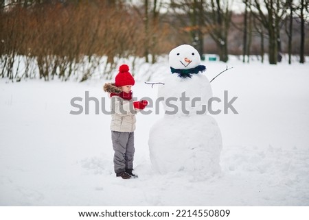 Adorable preschooler girl building a snowman on a day with heavy snowfall. Happy child playing with snow. Winter activities for kids