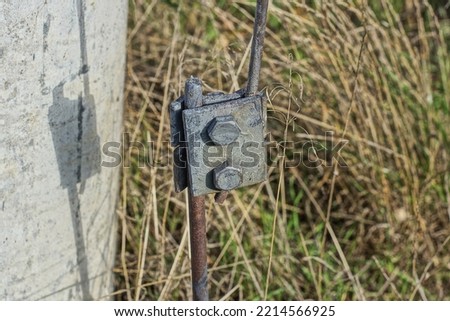 one brown rusty iron grounding rod near a gray concrete pillar in the grass on the street