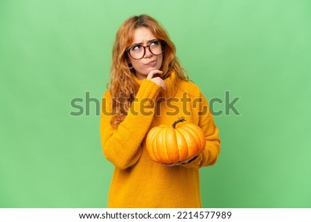 Young caucasian woman holding a pumpkin isolated on green screen chroma key background and looking up