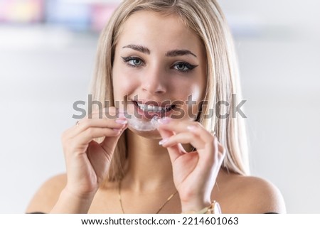 Portrait of beautiful young woman with perfect teeth   holding orthodontic retainers in dental clinic.