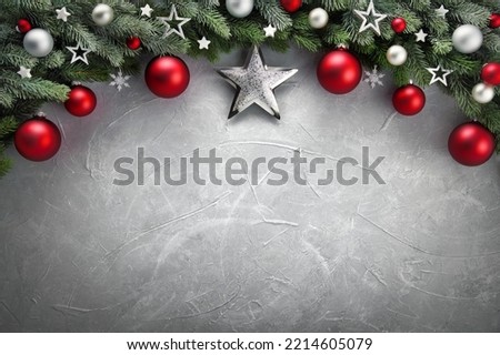 Elegant modern Christmas background with an arch-shaped border composed of fir branches, red and silver baubles and stars, on gray textured surface as copy space