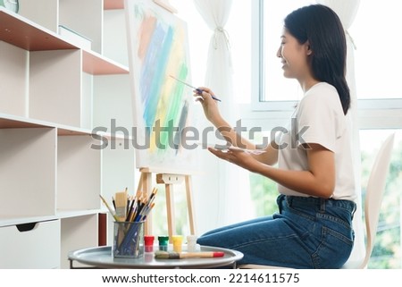 The art concept, Asian female artist using paintbrush to create masterpiece on canvas in art studio.