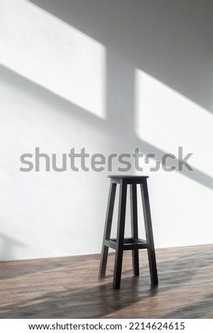 A white room with a shade from the sun through the window and one high bar stool. Minimalism style in horizontal photography. Loneliness concept with one chair and white space with shadows Royalty-Free Stock Photo #2214624615