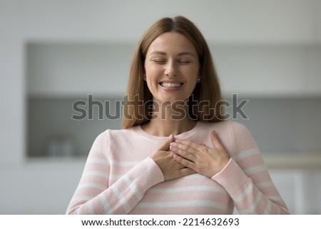 Headshot portrait young attractive woman holding folded palms on chest, close her eyes, express gratitude or praying, feels thankful, posing indoors, female volunteer showing kindness looking grateful Royalty-Free Stock Photo #2214632693