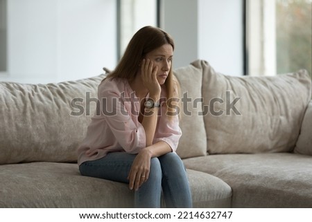 Sad lonely woman sits on sofa alone at home looks frustrated feel worried suffers from break up, having mental disorder, psychological concerns, need professional counsellor help, think about problems Royalty-Free Stock Photo #2214632747