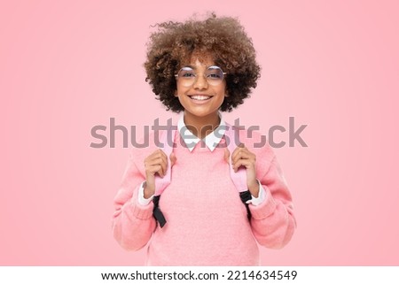 Studio portrait of smiling african american school girl or college student with curly afro hair and pink backpack, isolated on pink background