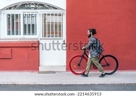 Bearded man walking with his cool bike in the street against red background.