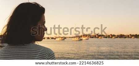 Young woman sitting alone on seaport coast, looking distant. High resolution photo image can be used as large printed canvas, website banner, social media post. Copy space for advertising.
