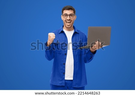 Screaming amazed winner holding laptop and celebrating success, isolated on blue background