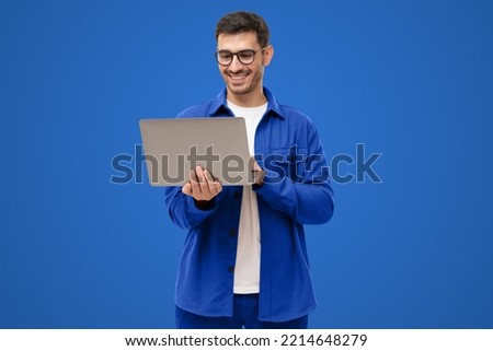 Young man holding laptop surfing, browsing online, typing message or watching movie isolated on blue background Royalty-Free Stock Photo #2214648279