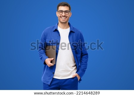 Young smiling modern man or male teacher holding laptop, isolated on blue background