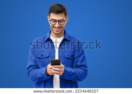 Young man looking at phone, standing isolated on blue background