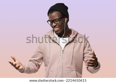 Horizontal shot of young handsome African guy isolated on purple background wearing casual clothes and black hat listening to music and dancing with earphones on having closed eyes with delight