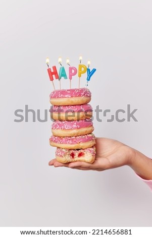 Vertical shot of unknown person holds pile of doughnuts with burning candles celebrates birthday or special occasion isolated over white background. Delicious glazed donuts in someones hand.