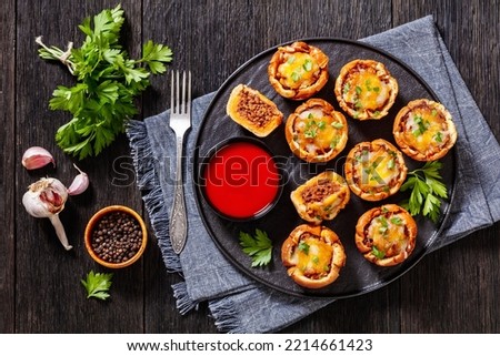 sloppy joe cups, hamburger bun cups with ground beef and onions tossed in sloppy joe sauce and topped with cheese on black plate on wood table, horizontal view from above, flat lay