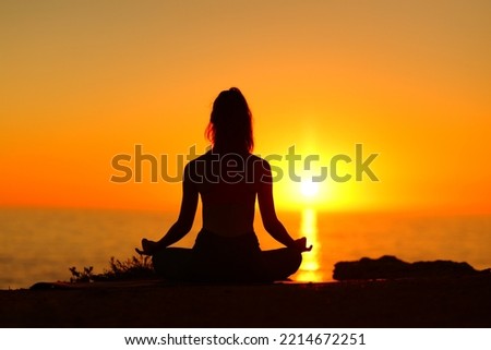 Back view portrait of a silhouette of a woman doing yoga with sunset sun Royalty-Free Stock Photo #2214672251