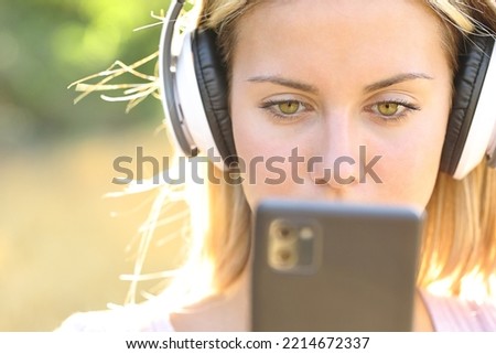 Front view portrait of a teen listening to music checking phone outside