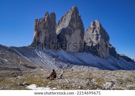Man backpacker hiking with her dog in Dolomites Alps mountains during sunny day