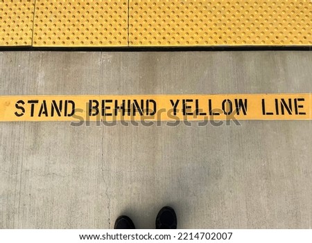 Sign stating Stand Behind Yellow line with a sight impaired barrier at a train station