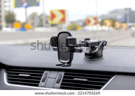 Phone holder on the car dashboard. Blurred view of traffic through the windshield