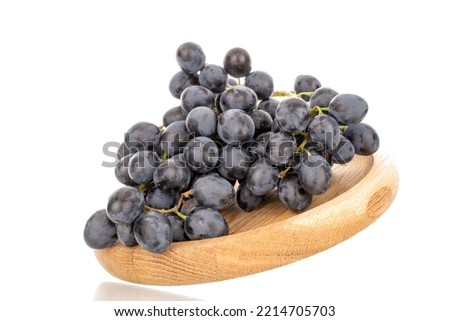 One sprig of sweet black grapes on a wooden plate, macro, isolated on white background.