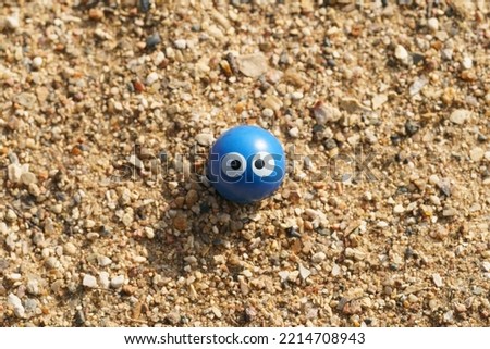 Sad emoticon icon. Blue toy ball. He's laid on the sand near the river. Cute sorrow line a human face. Close up photography. Concept of offending