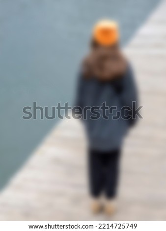 Defocus, abstract background. A girl in an orange hat stands on the pier. Royalty-Free Stock Photo #2214725749
