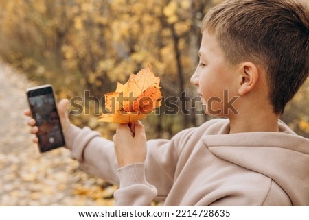 Teenager boy with autumn bouquet of maple leaves taking selfie photos with his smartphone.