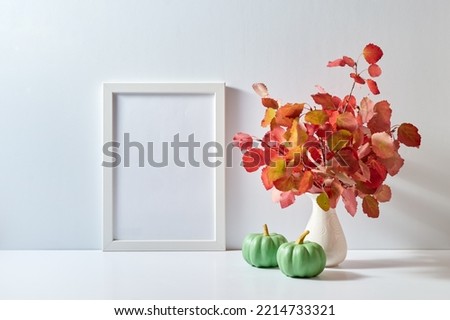 Mockup with a white frame and colorful autumn leaves in a vase, pumpkins on a light background. Empty poster frame mockup for presentation design, text, lettering