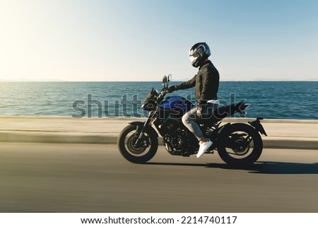 Side view of a motorcycle rider riding race motorcycle on a sea background with motion blur Royalty-Free Stock Photo #2214740117