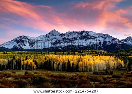 Dramatic sunset with pink and orange clouds over snow covered Mount Wilson near Telluride Colorado with changing yellow Aspen trees in foreground on cool fall evening Royalty-Free Stock Photo #2214754287