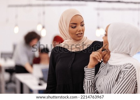 Two African American muslim female colleagues with hijab in a modern office space. Group of people working in the background Diversity and success concept.