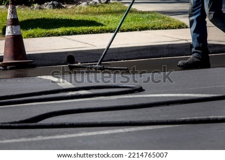 Worker using a sealcoating brush during asphalt resurfacing project  Royalty-Free Stock Photo #2214765007