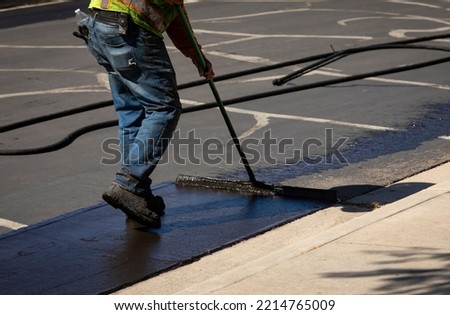 Worker using a sealcoating brush during asphalt resurfacing project  Royalty-Free Stock Photo #2214765009