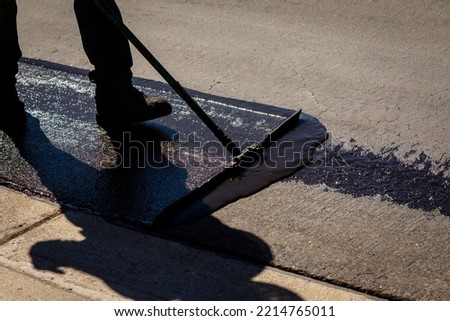 Worker using a sealcoating brush during asphalt resurfacing project  Royalty-Free Stock Photo #2214765011