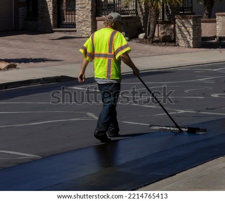 Worker using a sealcoating brush during asphalt resurfacing project  Royalty-Free Stock Photo #2214765413