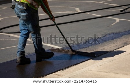 Worker using a sealcoating brush during asphalt resurfacing project  Royalty-Free Stock Photo #2214765415