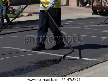 Worker spraying slurry tar on street during resurfacing project  Royalty-Free Stock Photo #2214765421