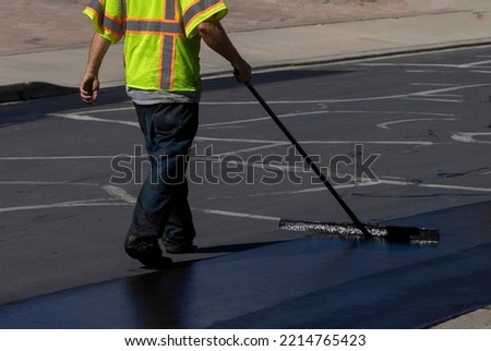 Worker using a sealcoating brush during asphalt resurfacing project  Royalty-Free Stock Photo #2214765423