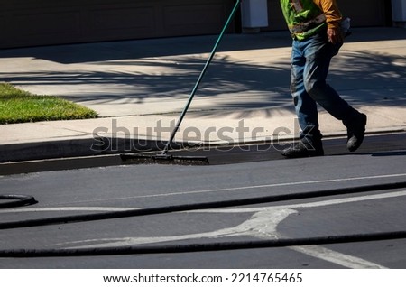 Worker using a sealcoating brush during asphalt resurfacing project  Royalty-Free Stock Photo #2214765465