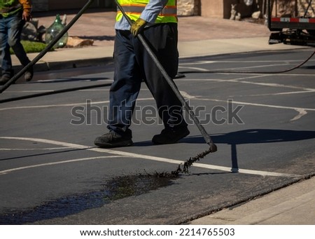 Worker spraying slurry tar on street during resurfacing project  Royalty-Free Stock Photo #2214765503