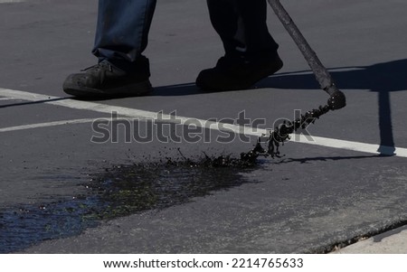 Worker spraying slurry tar on street during resurfacing project  Royalty-Free Stock Photo #2214765633