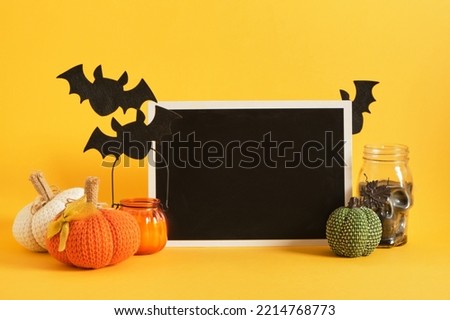 mocap black plate and halloween decor on a bright yellow background, candles, felt bats, knitted and fabric homemade pumpkins for holiday decoration, space for text, advertising, invitations