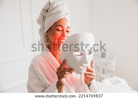 Beautiful young woman getting a led light therapy mask treatment  for her face at the beauty salon.