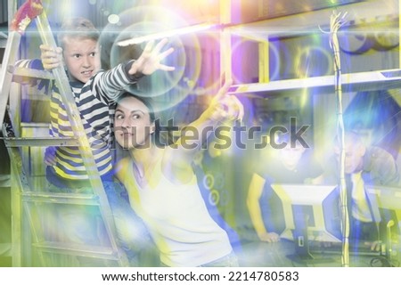 Young woman with her preteen son reaching for something in quest room designed as underground shelter. Toned image