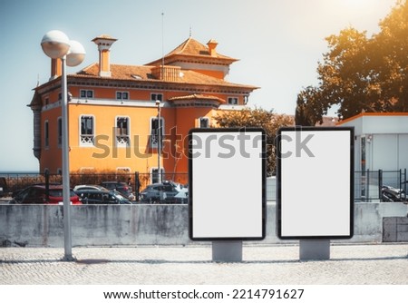 Two empty mock-ups of street advertising billboards on the pavement; two blank ad placeholders outdoors; template of outdoor advert posters on the paving stone in front of an orange house Royalty-Free Stock Photo #2214791627