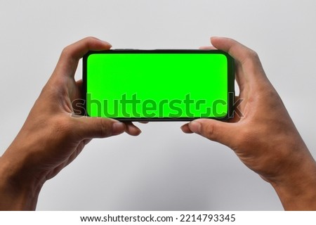Man holds in two hands smartphone in landscape mode with green screen isolated on white background.
