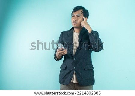 Asian businessman wearing black suit looks thoughtful while holding smart phone. standing on a blue background