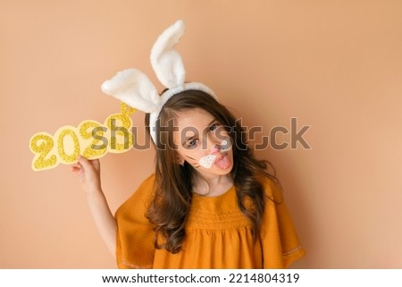 An attractive gorgeous girl in the guise of a rabbit - the symbol of the new year, holds the number 2023 in hand and shows her tongue
