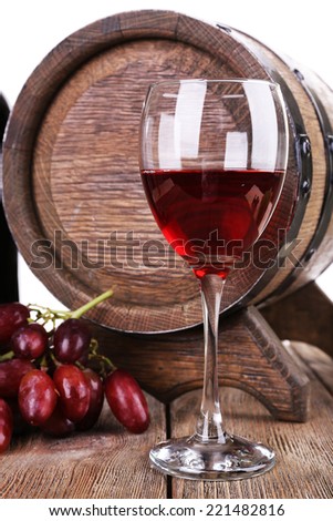 Red wine in goblet, grapes and barrel on wooden table on white background